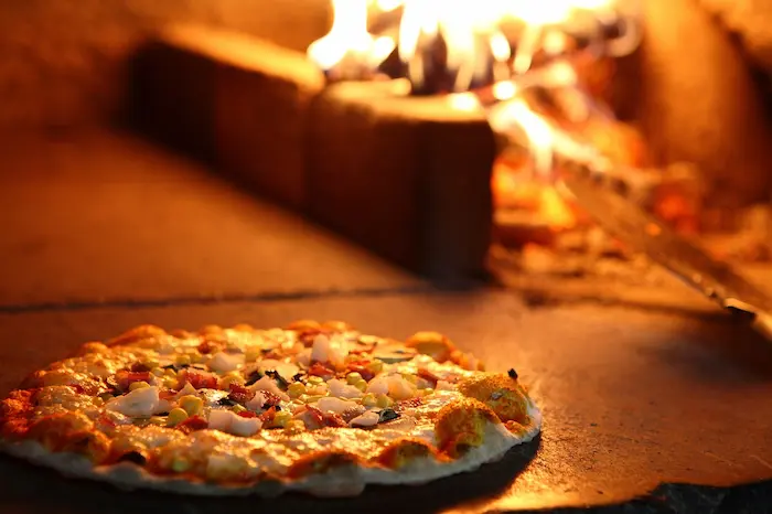 A fiery pizza oven with a bubbling pizza ready to come out